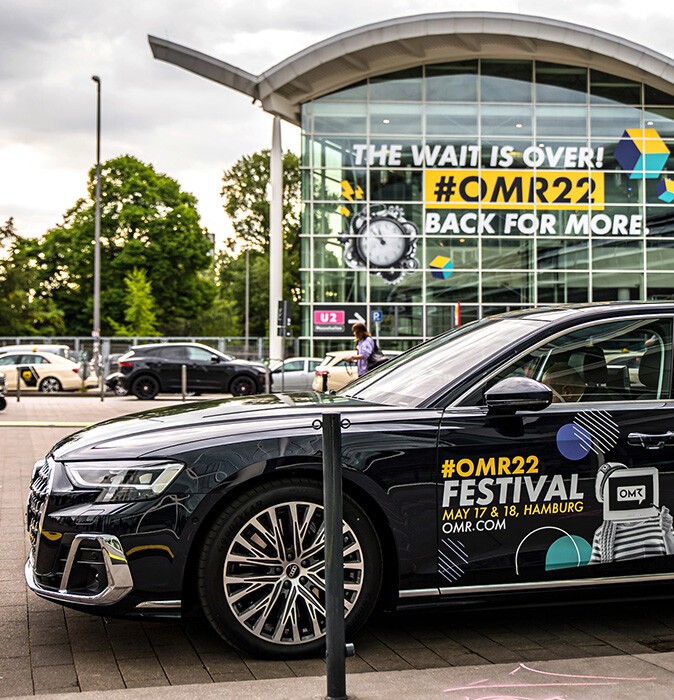 A black car with OMR lettering, standing in front of the exhibition halls during OMR2022