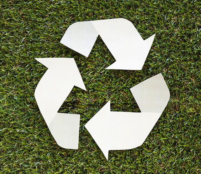 A white recycling logo lying on short grass